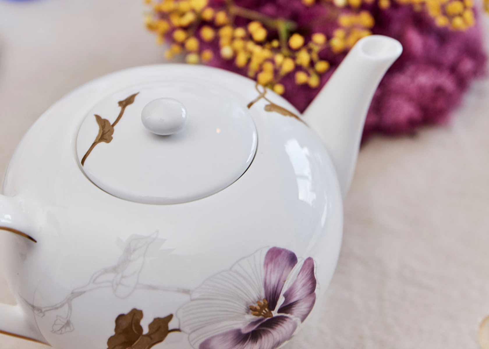 The Flora Teapot seen in a close up from above standing on a table next to some pink flowers